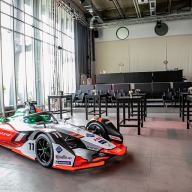 Der Saal bei einer Vernstaltung von Audi-Sport. im Vordegrund steht ein Audi Formula E Rennwagen. Die Bestuhlung des Saals besteht aus Hochtischen und wenigen Reihen mit Bequemen Lederstühlen.