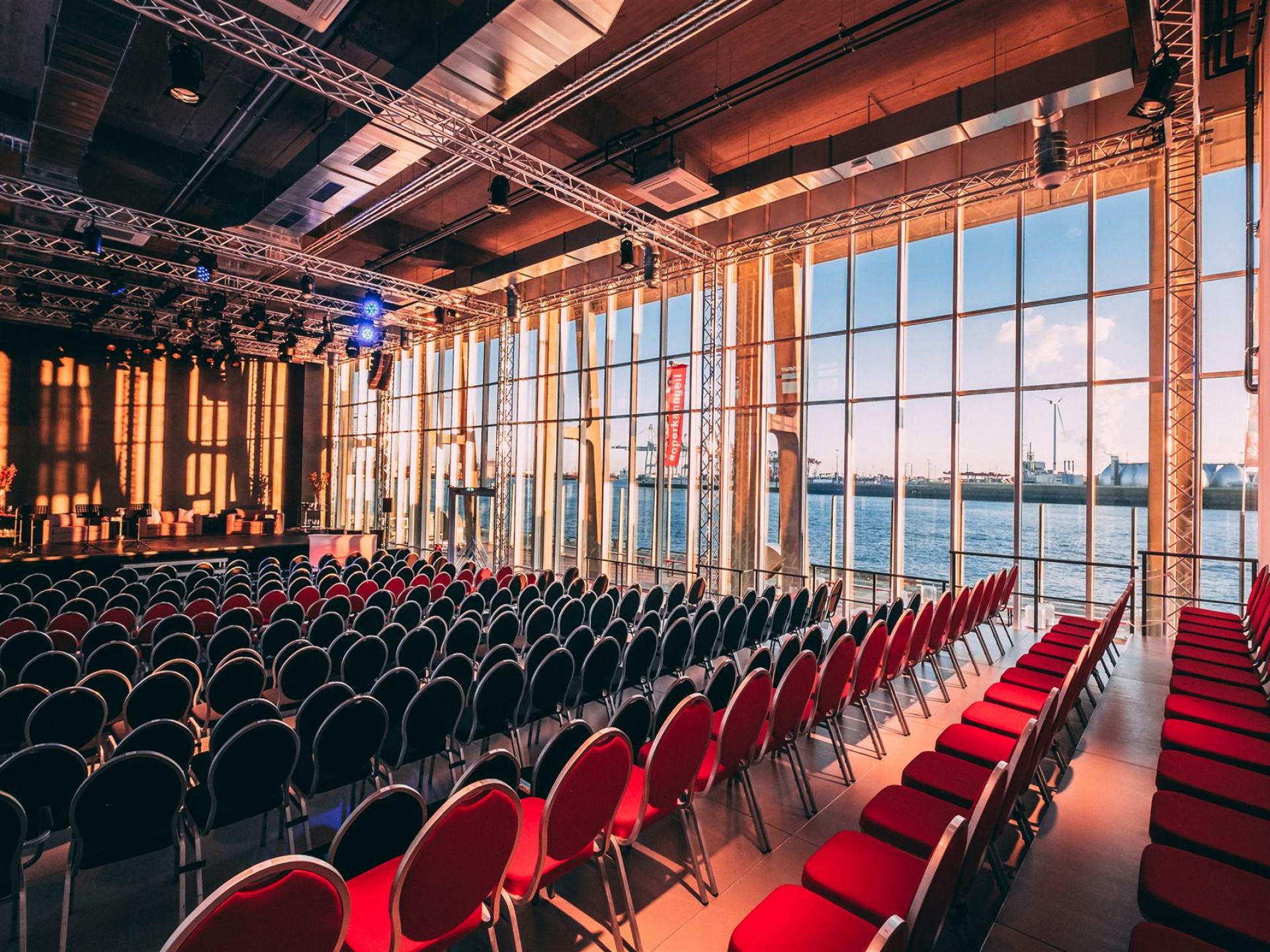 Der Saal des Opernlofts in normaler Bestuhlung mit frontaler Bühne. Auf der rechten Seite des Saals kann man durch die Fensterfront den Hafen sehen.