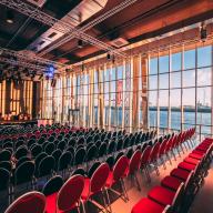Der Saal des Opernlofts in normaler Bestuhlung mit frontaler Bühne. Auf der rechten Seite des Saals kann man durch die Fensterfront den Hafen sehen.
