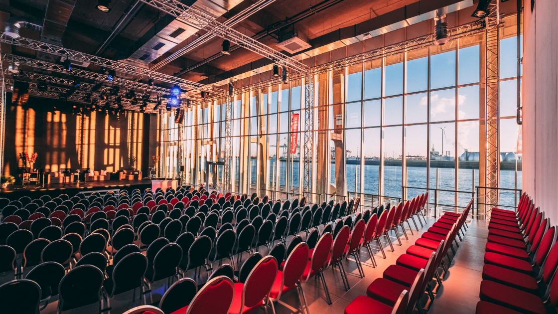 Der Saal des Opernlofts in normaler Bestuhlung mit frontaler Bühne. Auf der rechten Seite des Saals kann man durch die Fensterfront den Hafen sehen.