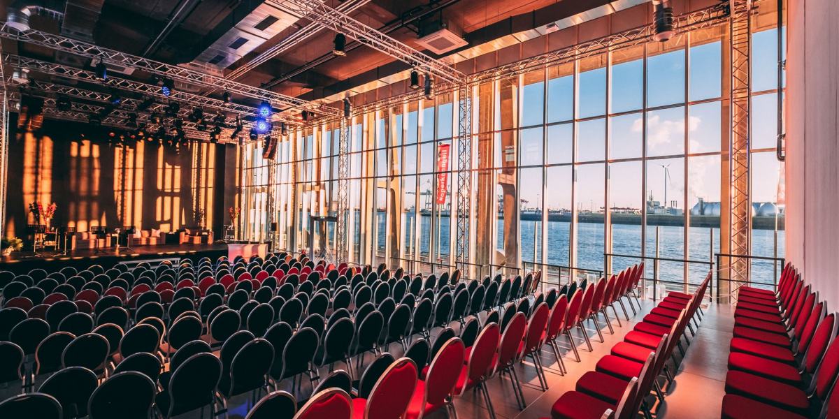 Der Saal des Opernlofts in normaler Bestuhlung mit frontaler Bühne. Auf der rechten Seite des Saals kann man durch die Fensterfront den Hafen sehen.