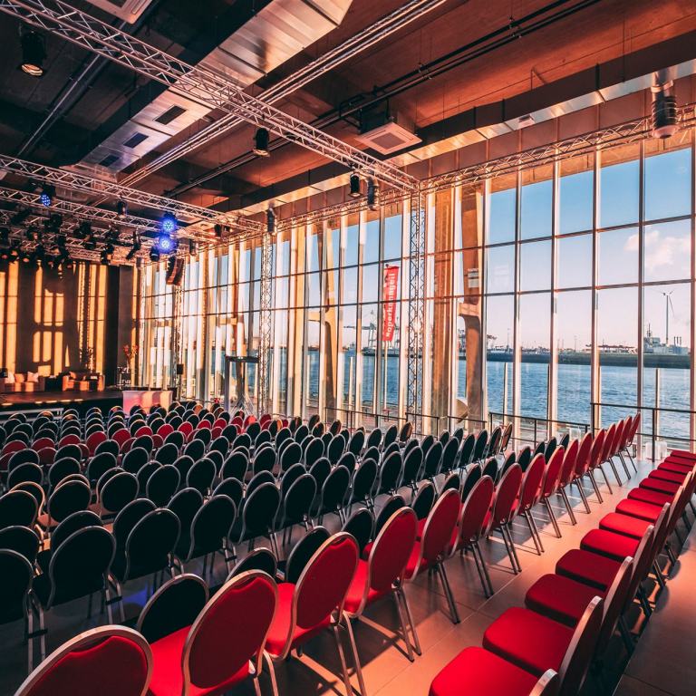 Der Saal des Opernlofts in normaler Bestuhlung mit frontaler Bühne. Auf der rechten Seite des Saals kann man durch die Fensterfront den Hafen sehen.